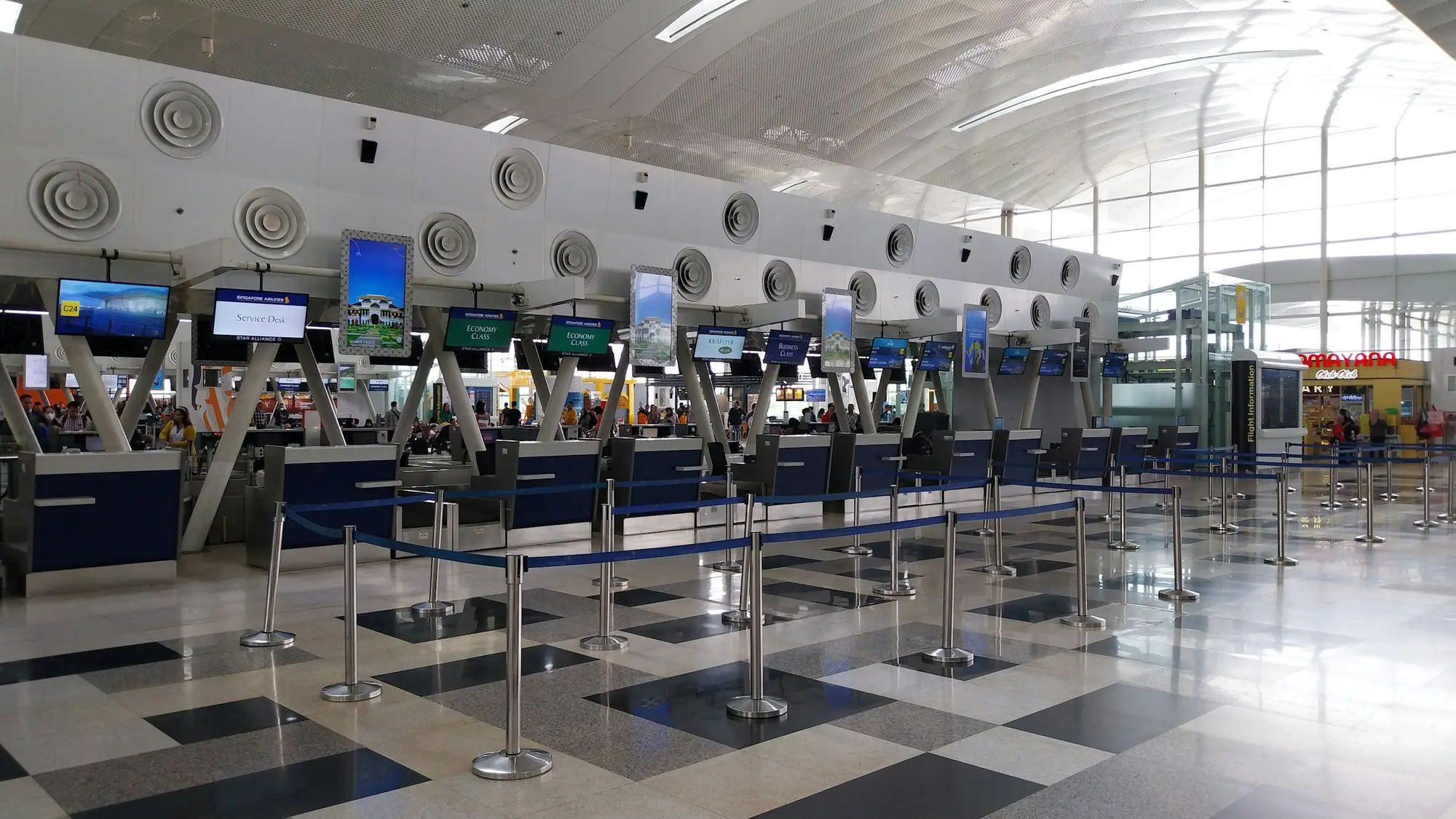 A row of empty airline check-in and bag-drop counters with queue barriers inside an airport terminal.