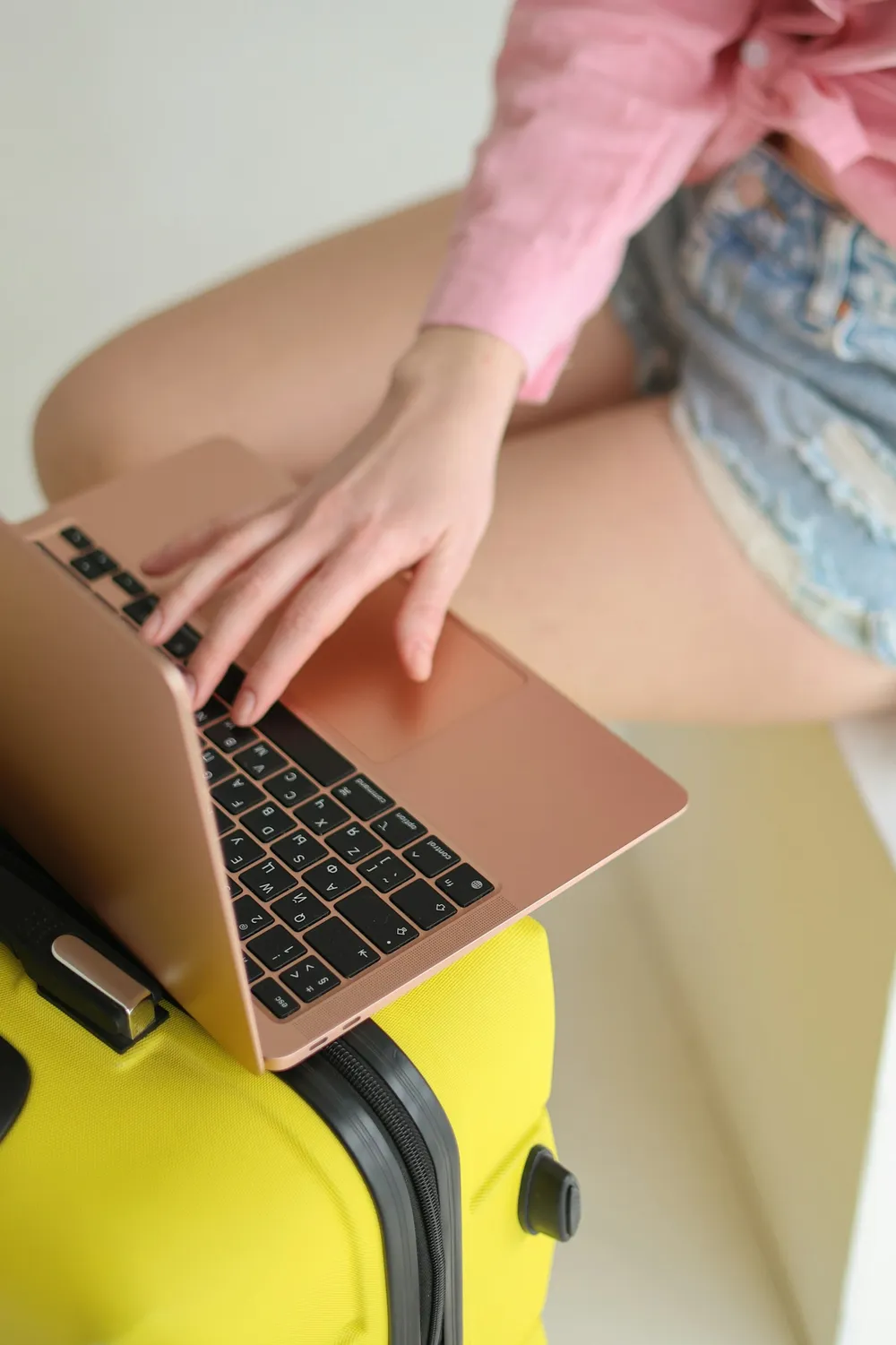 Hands typing on a laptop resting on a suitcase while searching for flights.