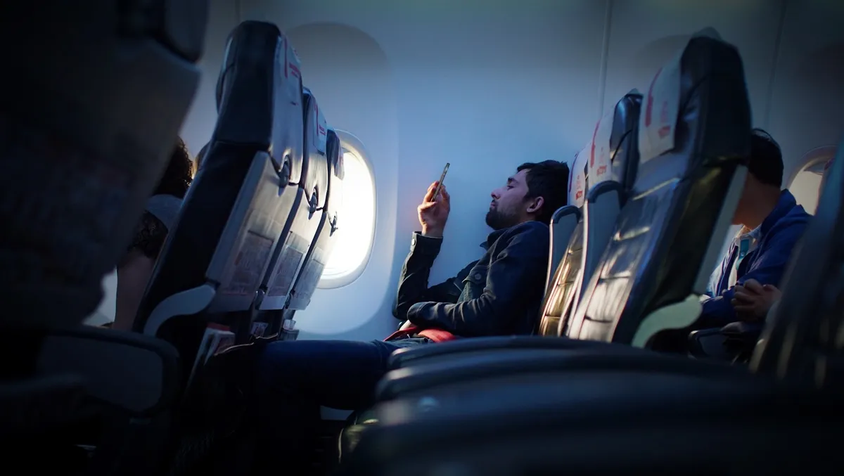 A traveler checking his phone while seated on a plane by the window.