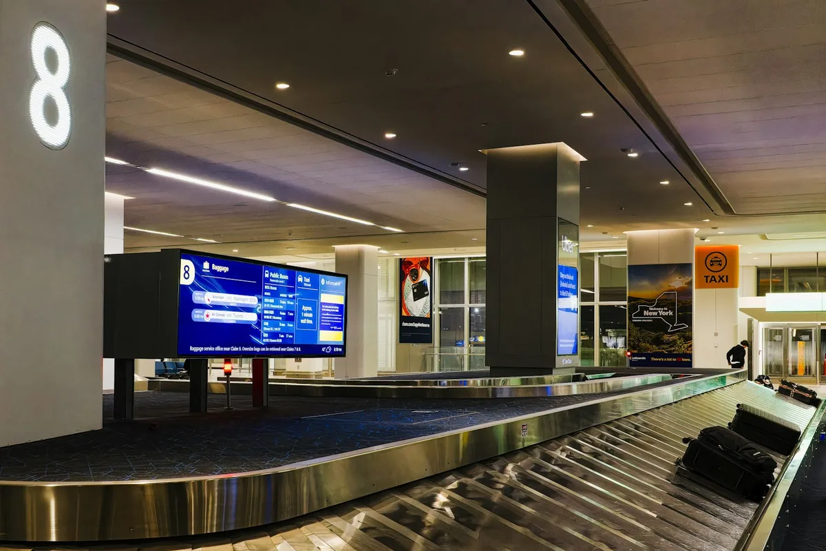 Suitcases circling on an airport baggage-claim carousel beneath a large flight-information screen