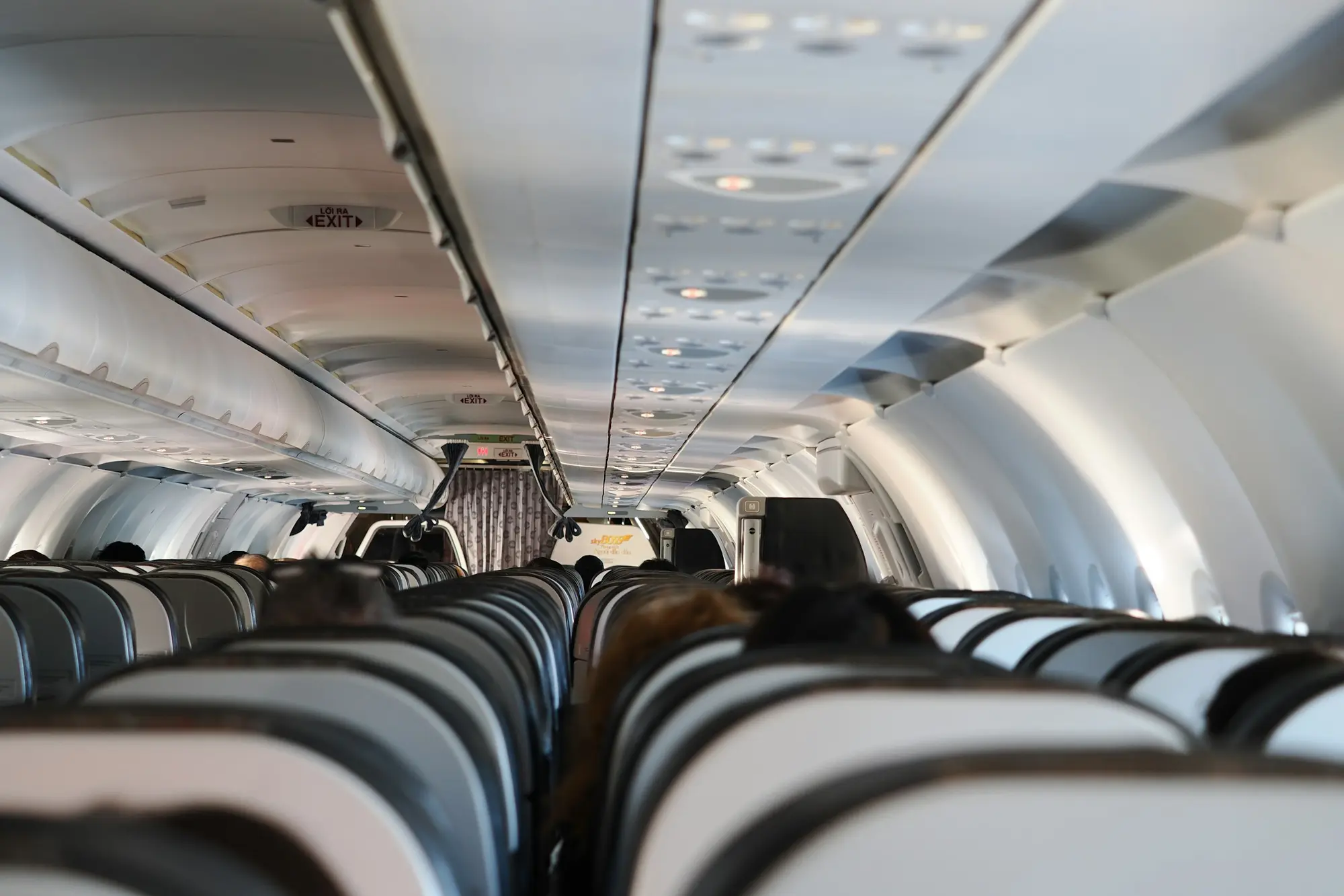 Rows of economy class airplane seats viewed from the aisle with overhead bins overhead