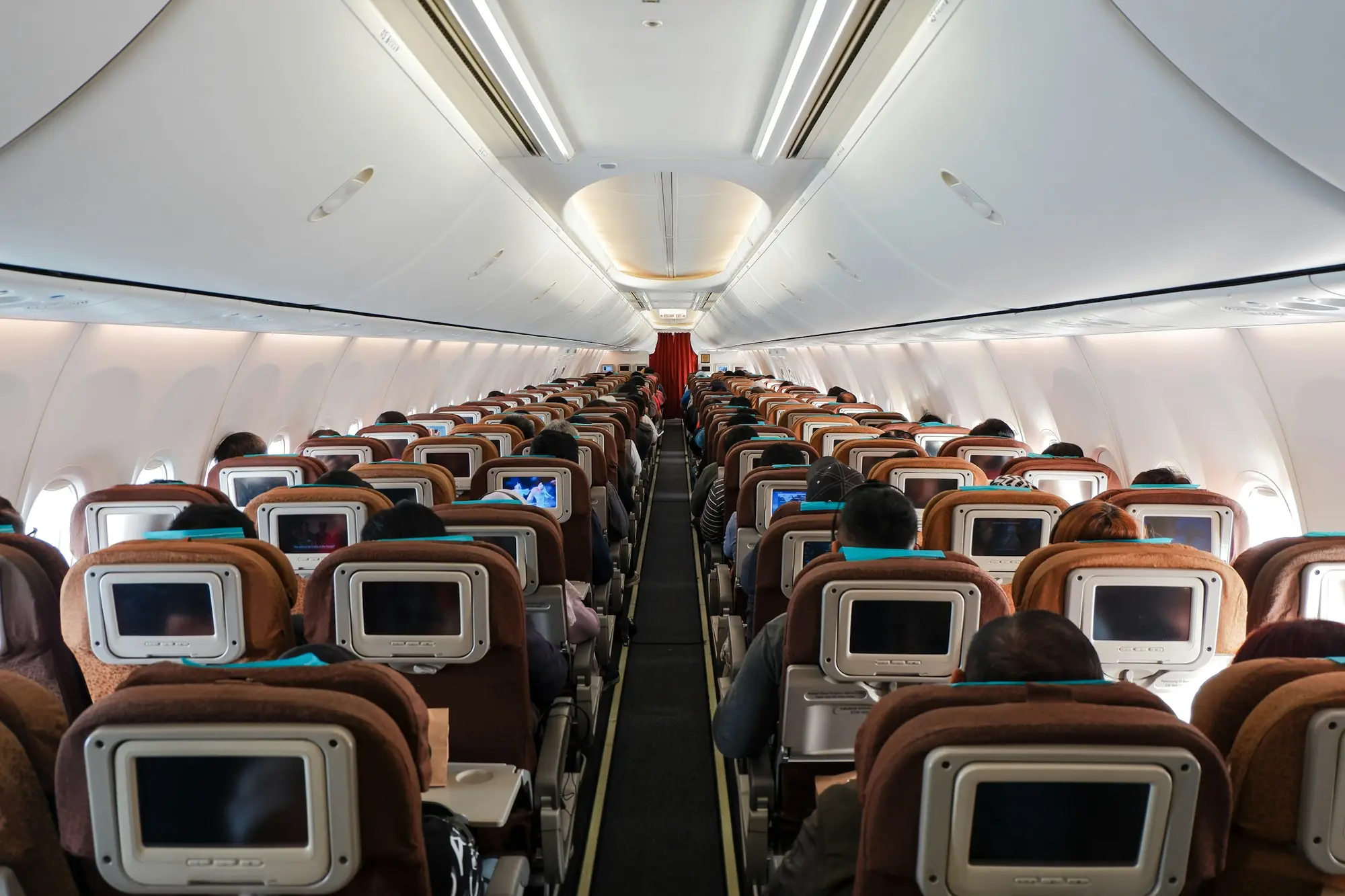 Economy class seats in an airplane cabin, viewed from the aisle with overhead bins visible