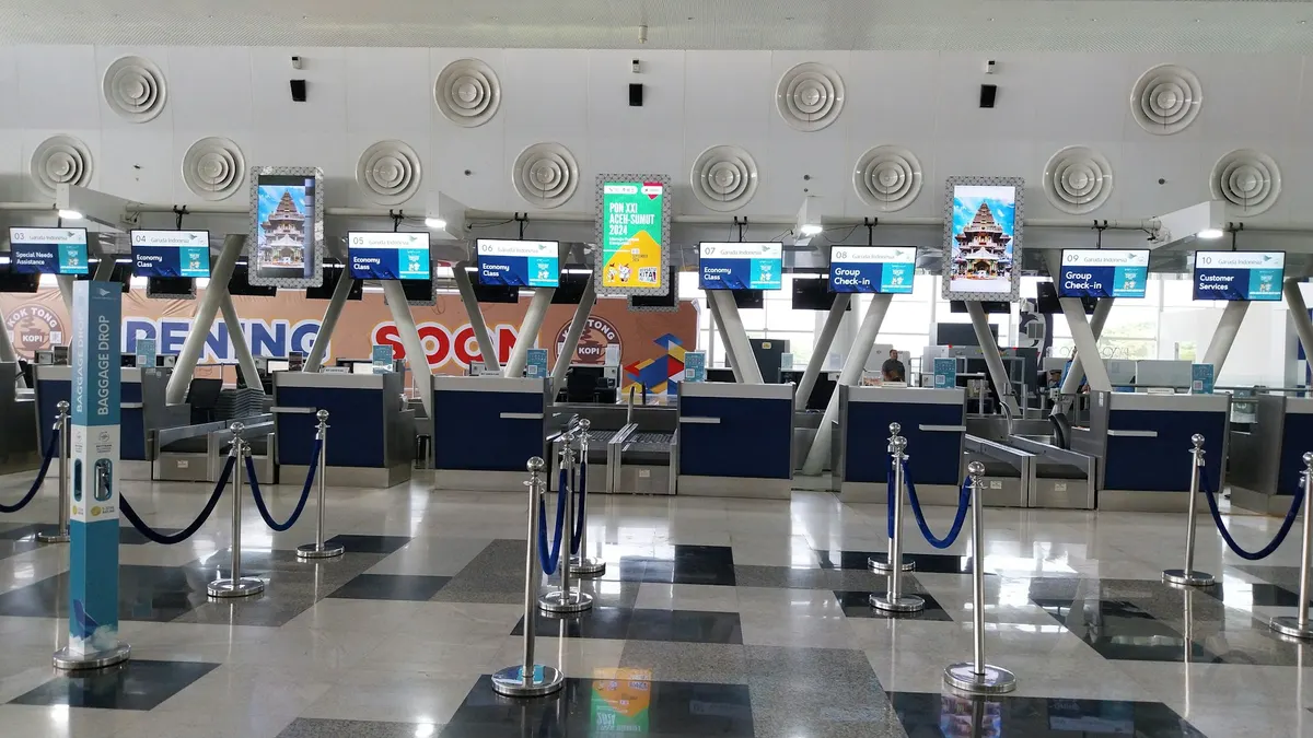 A row of empty airline check-in and bag-drop counters with queue barriers inside an airport terminal.